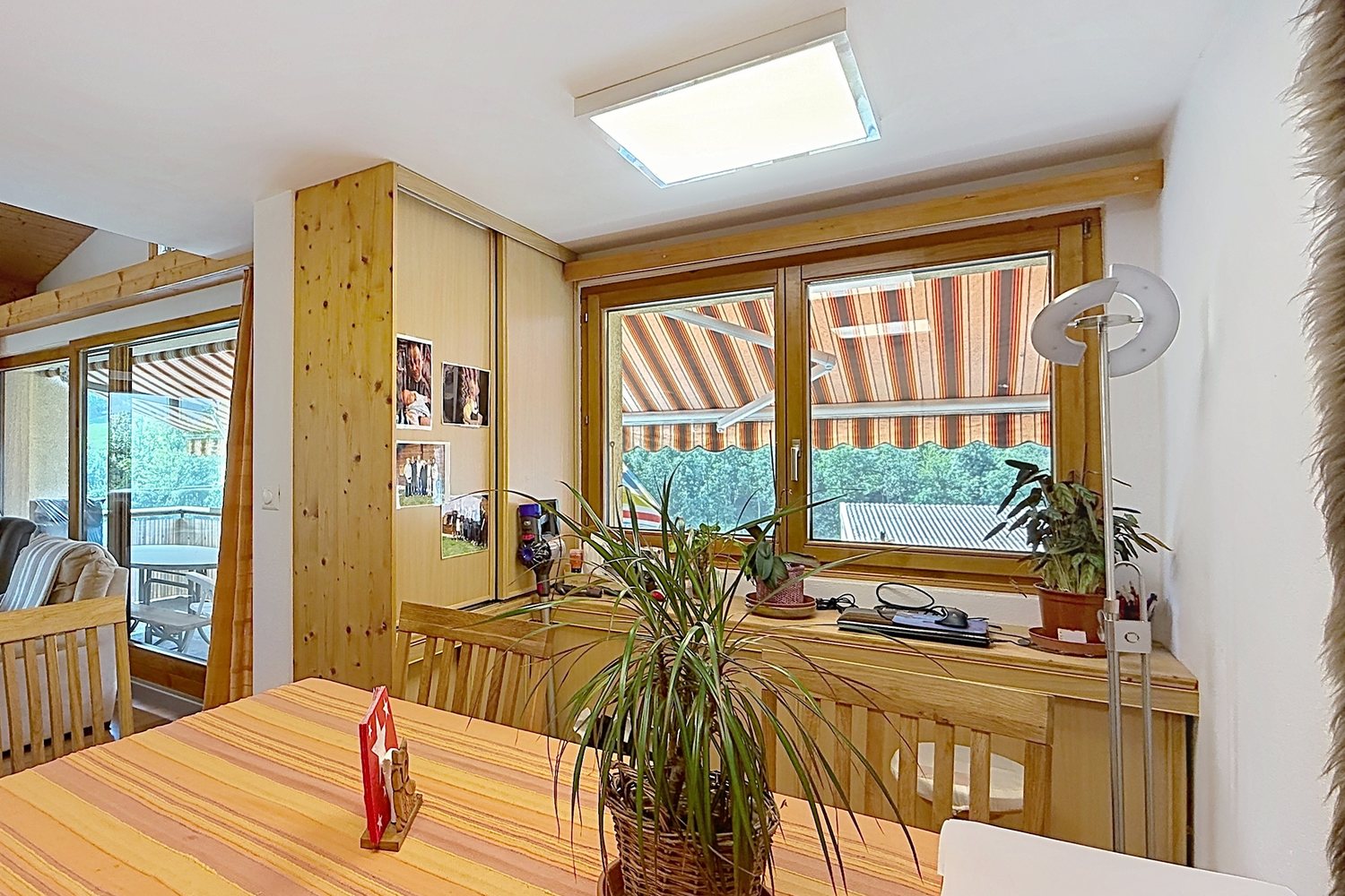 Salle à manger du duplex avec table en bois massif, fenêtre sur le balcon et séjour en arrière-plan.