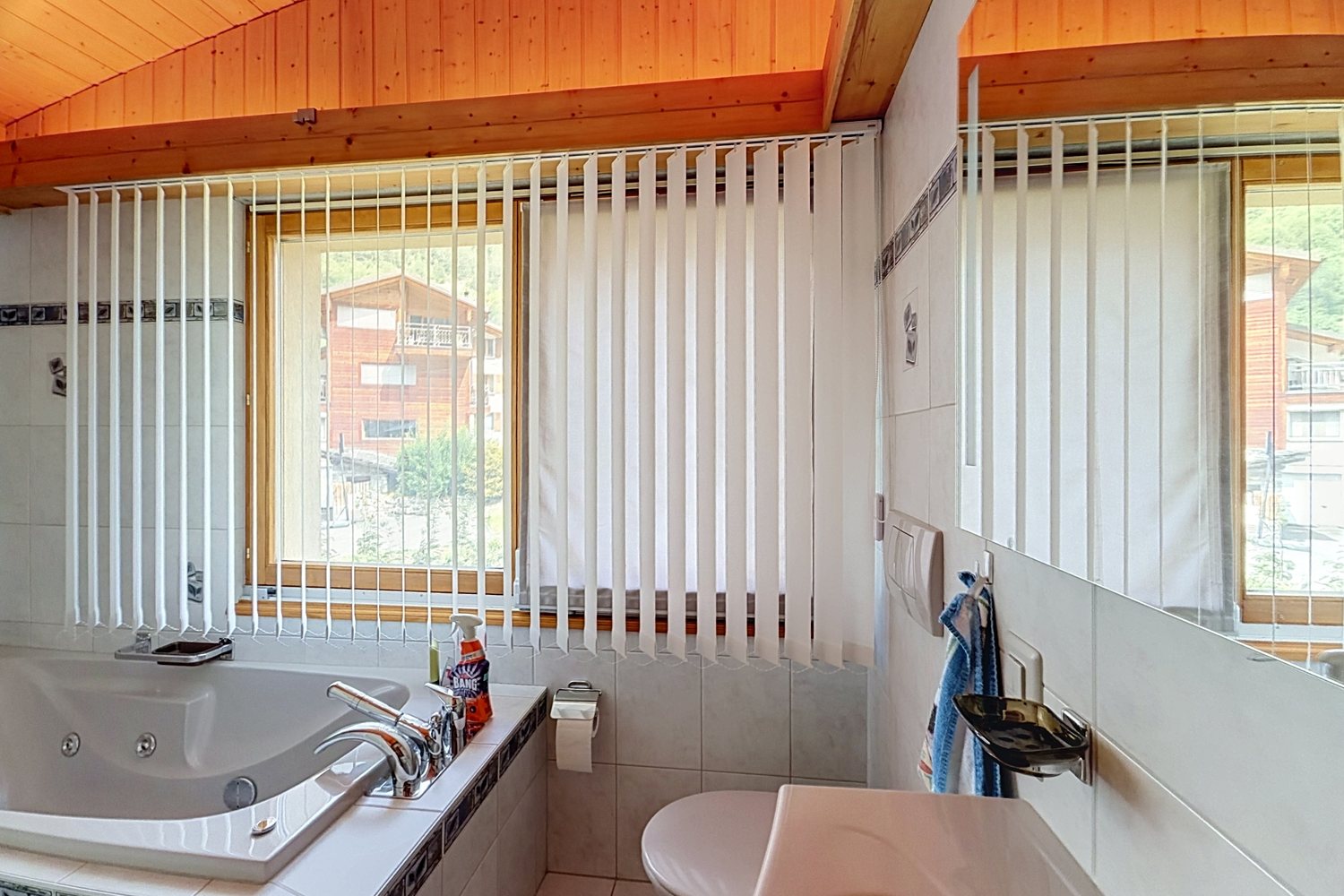 Salle de bains du duplex avec baignoire d'angle et fenêtre à stores verticaux.
