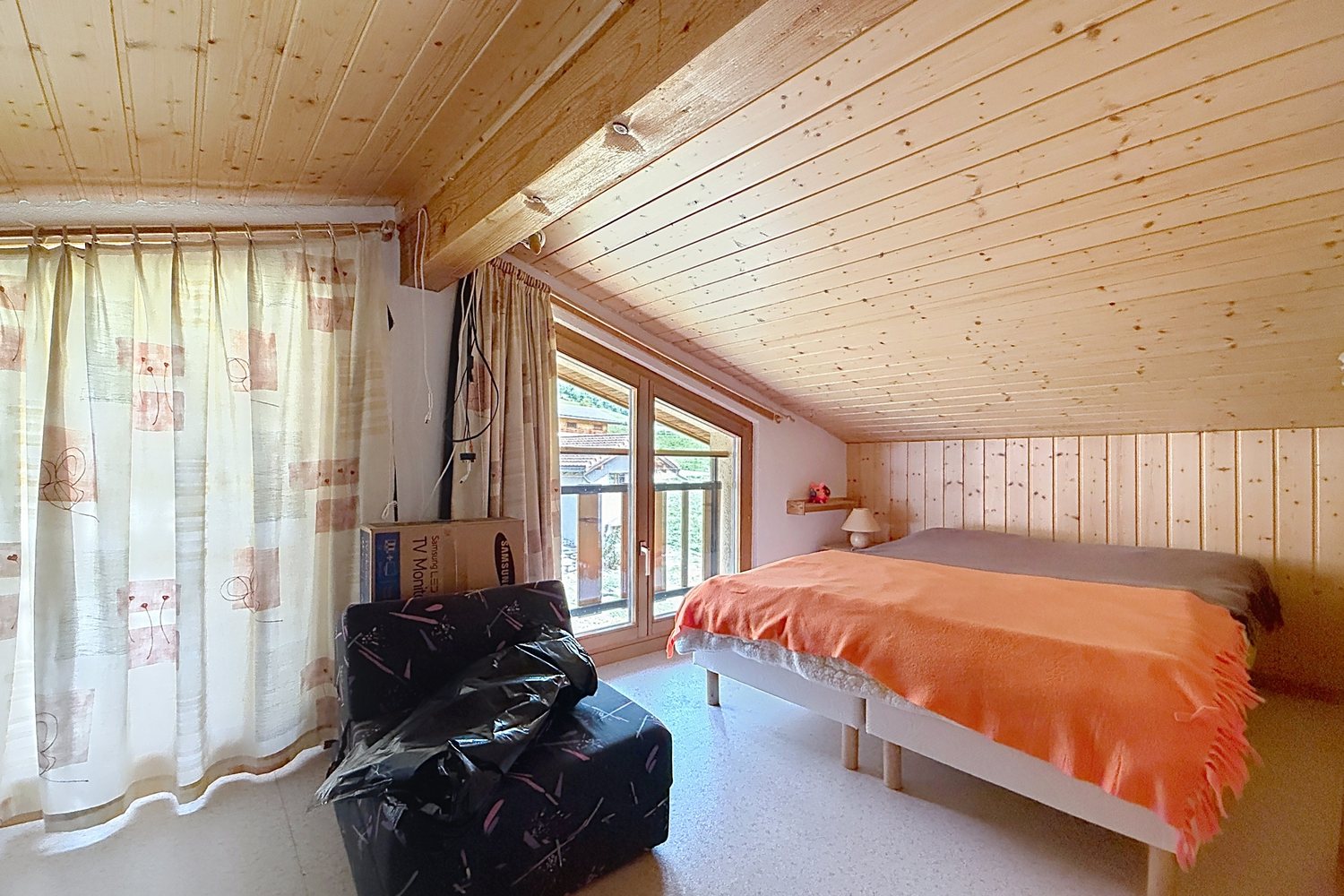Chambre sous le toit, en galerie, avec lit simple, lambris et porte-fenêtre sur le balcon.