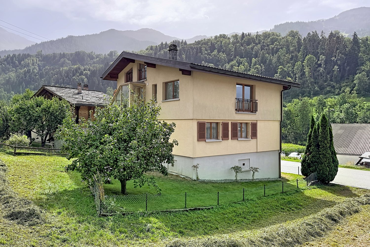 La maison vue depuis le jardin, avec un arbre fruitier au premier plan et les versants boisés derrière.