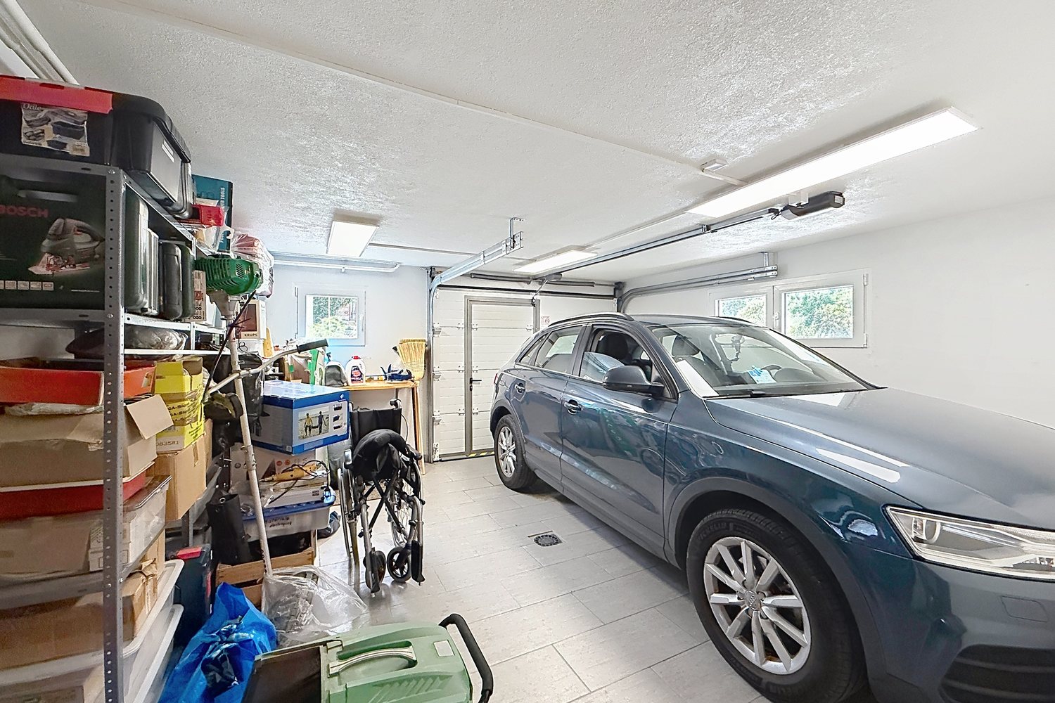 Garage du rez avec une voiture, étagères de rangement et porte sectionnelle.